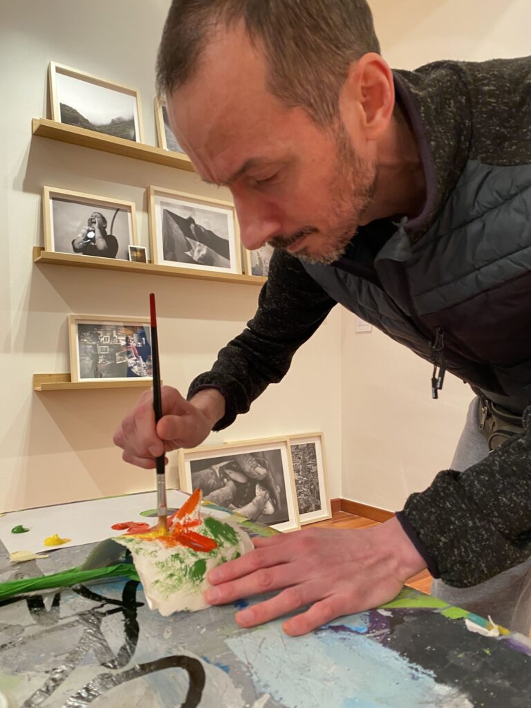 Un uomo dipinge una maschera con colori acrilici su un tavolo da lavoro.