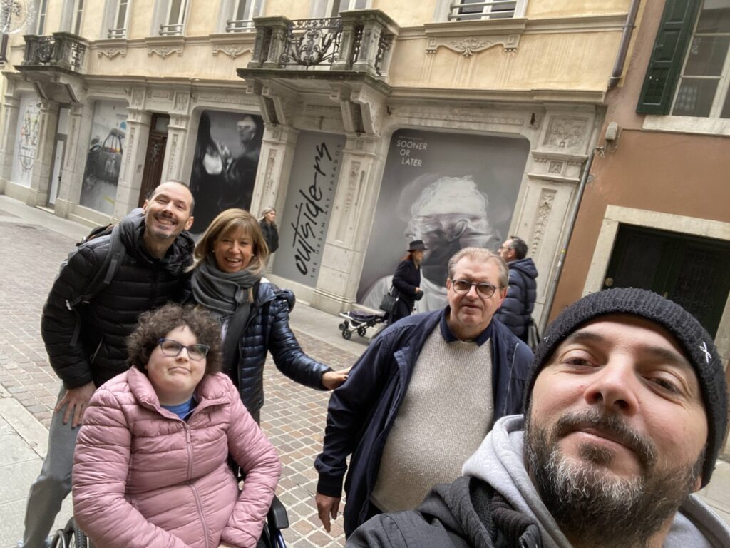 Gruppo di persone sorridenti in una strada cittadina, davanti a edifici storici.