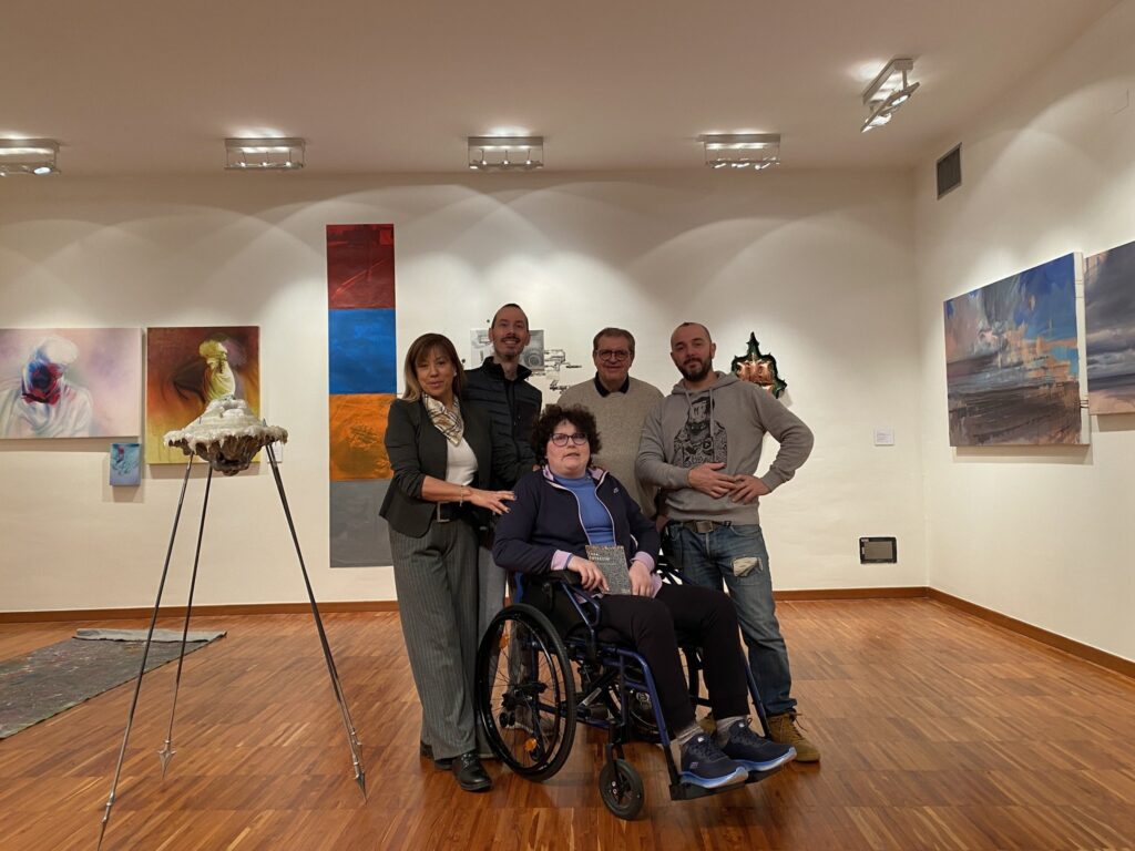 Gruppo di persone posa in una galleria d’arte, circondato da opere esposte.