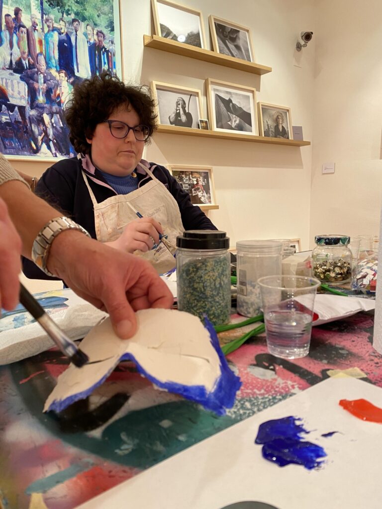 Persona dipinge una maschera durante un laboratorio artistico.