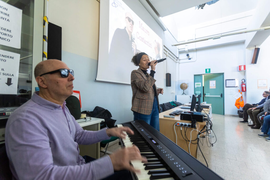 Mauro Costantini suona il piano elettrico mentre una cantante lo accompagna al microfono durante uno dei momenti musicali dell'incontro a scuola.