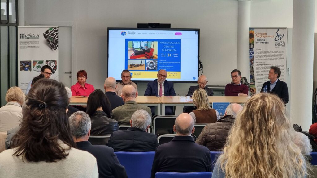 Vista frontale della conferenza con pubblico, relatori e banner della Comunità Piergiorgio