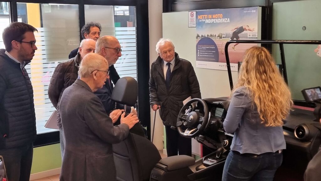 I partecipanti osservano il simulatore di guida del Centro di Mobilità con il poster "Metti in moto la tua indipendenza"