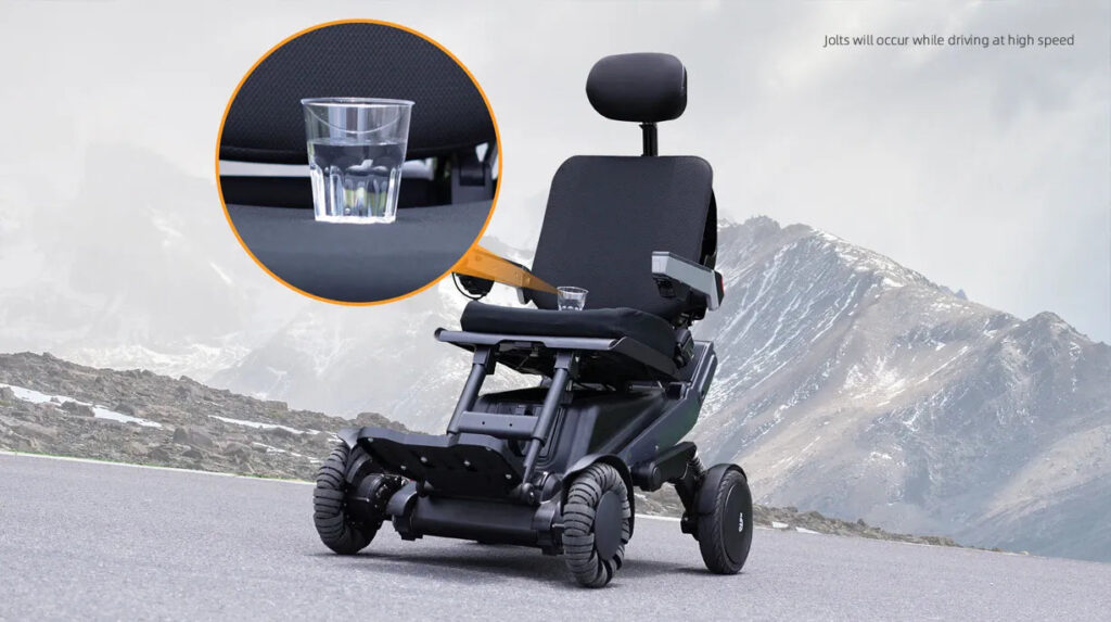 Carrozzina elettrica X12 su strada di montagna, con dettaglio di un bicchiere d’acqua per mostrare la stabilità durante la guida.