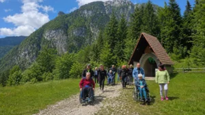 Gruppo di persone con volontari e carrozzine lungo un sentiero di montagna vicino alla Cappella Florit