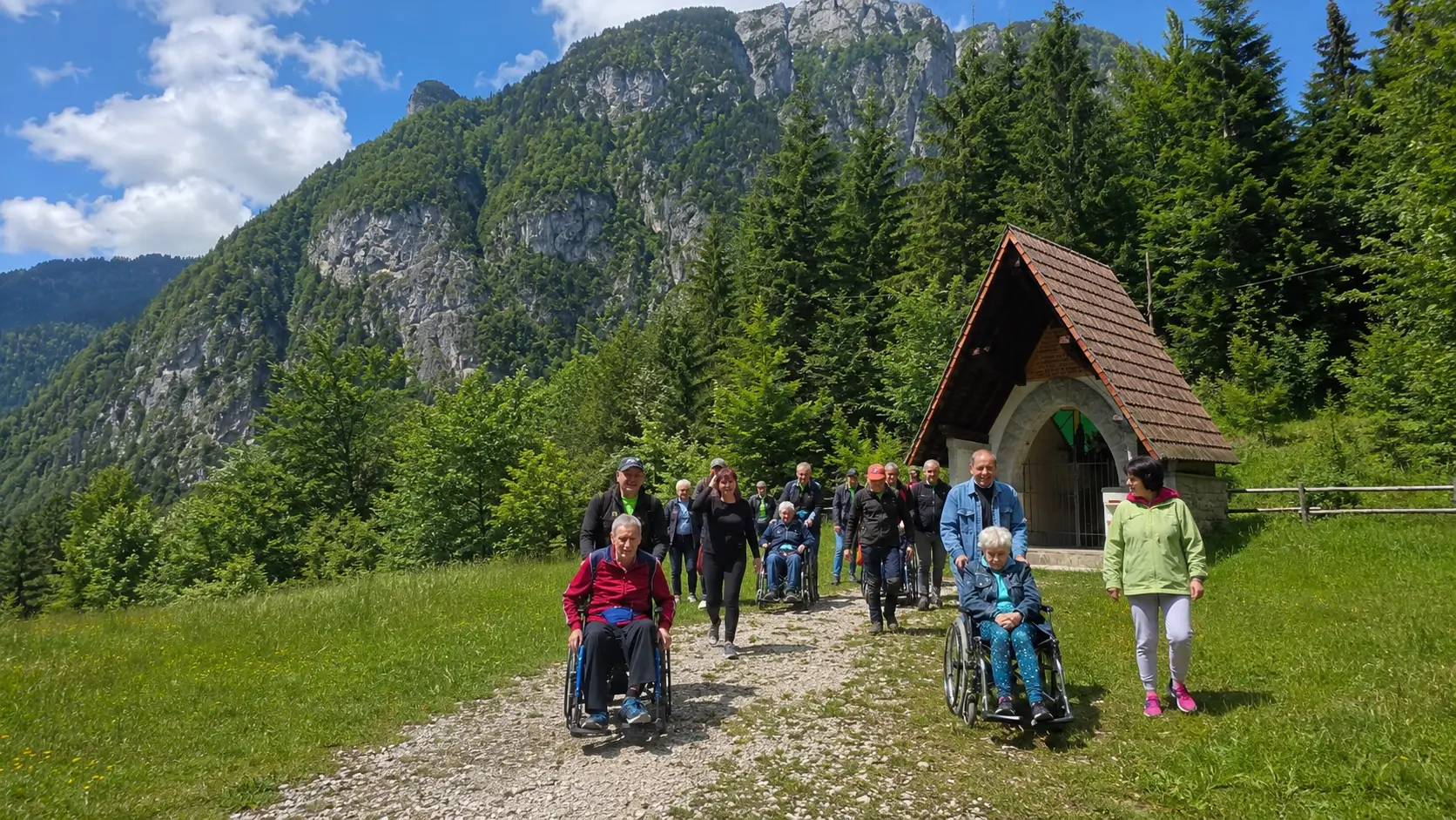 Gruppo di persone con volontari e carrozzine lungo un sentiero di montagna vicino alla Cappella Florit