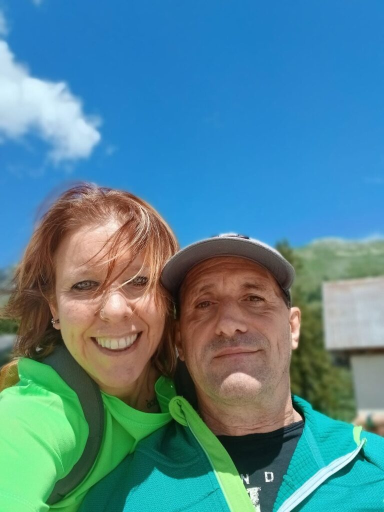 Selfie sorridente di una volontaria e un partecipante sotto il cielo azzurro del Montasio