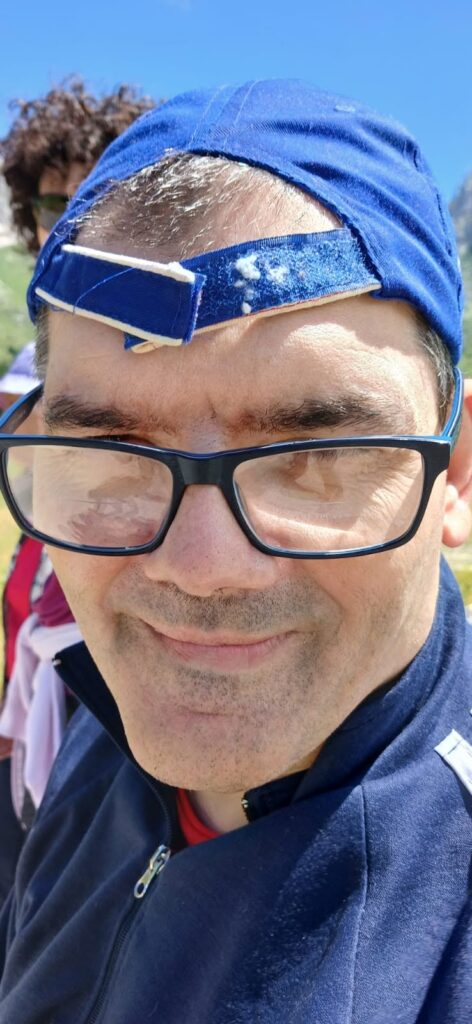 Primo piano di un partecipante sorridente con cappellino e occhiali durante l'escursione al Montasio