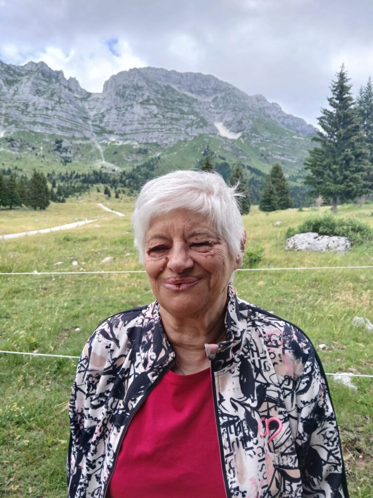 Partecipante sorridente sui prati dell'Altopiano del Montasio, con le vette delle Alpi Giulie alle spalle