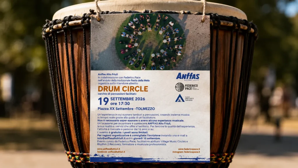 Locandina del Drum Circle del 19 settembre 2026 a Tolmezzo appesa a un grande tamburo djembe all'aperto.